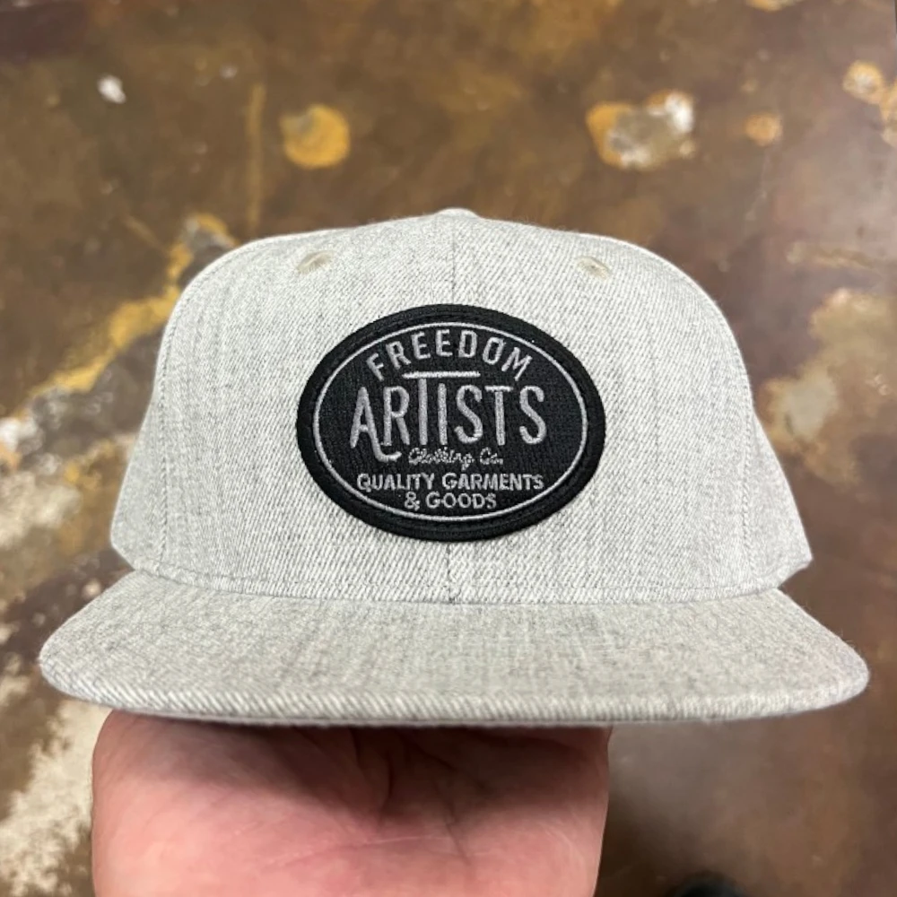 heather grey Yupoong 6089M flat bill snapback hat with black oval embroidered patch