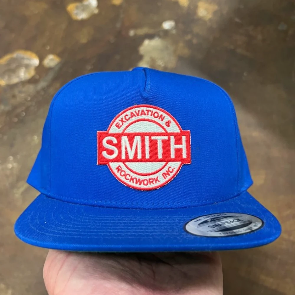 royal blue Yupoong 6007 flat bill snapback hat with red and white round embroidered patch