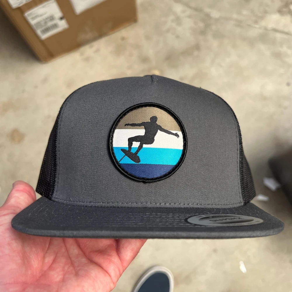 charcoal Yupoong 6006 mesh-back flat bill hat with round woven surfer patch