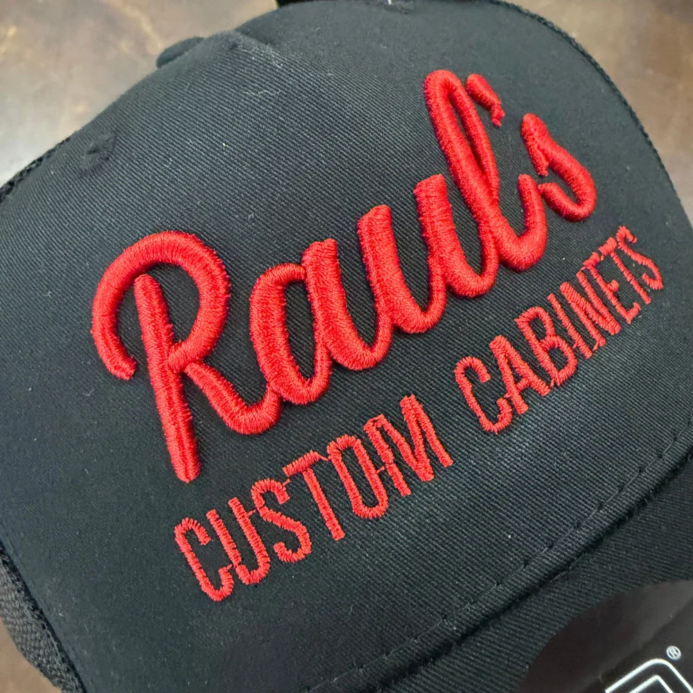Red 3D puff embroidery script logo on a black trucker hat