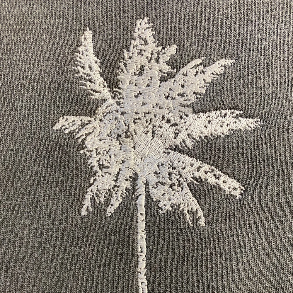 White palm tree embroidered on a gray hoodie with textured fill stitching
