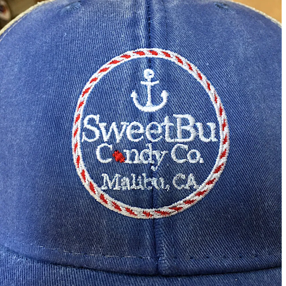 Multicolor embroidered circle logo on a washed blue trucker hat