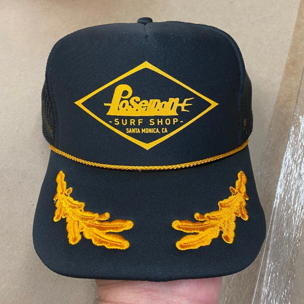 Black Otto Cap foam front trucker hat with gold rope, embroidered gold leaf visor, and printed logo